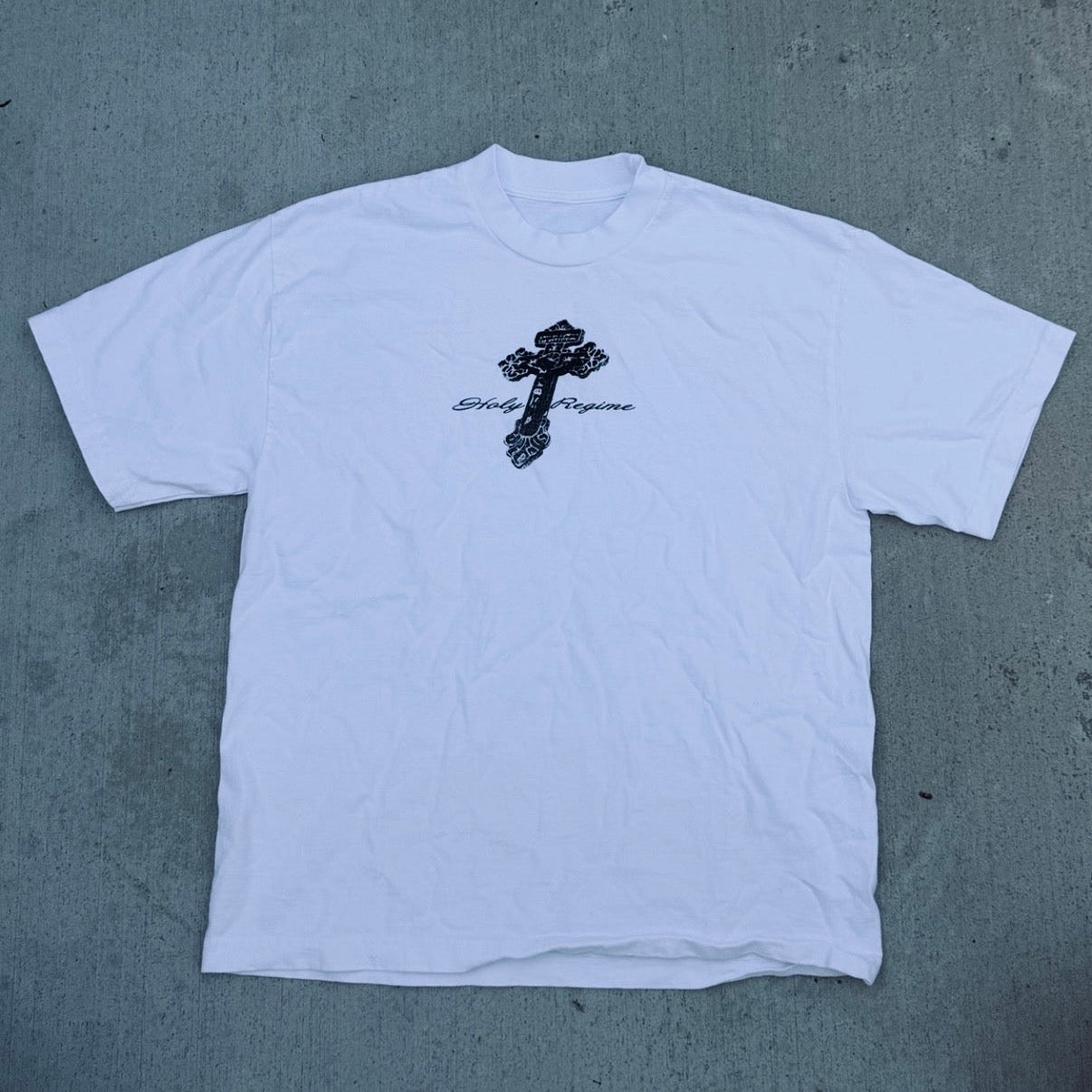 White t-shirt with a black cross design and text on a gray surface